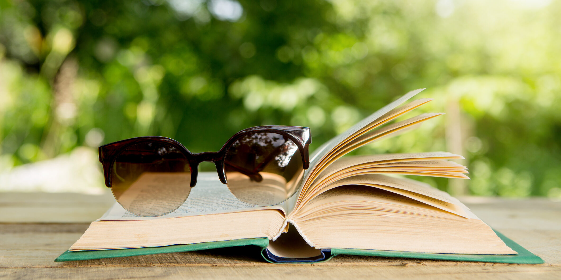 Open book and eyeglasses on a wooden table in a garden on a Sunny summer day