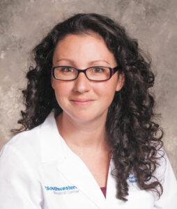 Headshot of pulmonologist Bethany Lussier with curly dark hair and glasses wearing a white medical coat against a neutral background.
