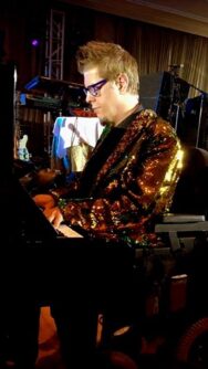 A man in a sparkly coat performs on stage