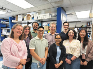 Thomas Cooper and his research team pose together in a laboratory surrounded by shelves of scientific supplies.