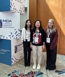 Asuka Eguchi and two members of her lab team pose beside signage at the MDA Clinical & Scientific Conference.