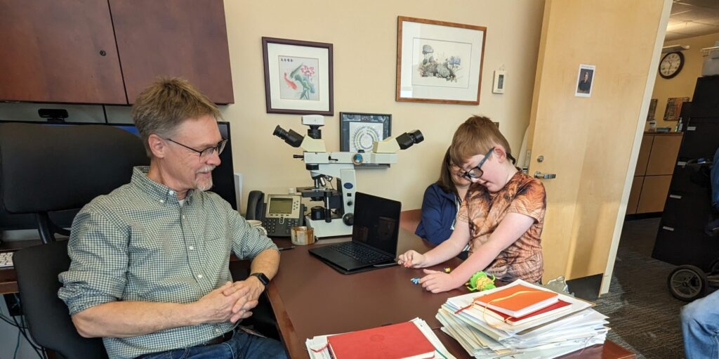 Doctor speaking with a child and caregiver in a medical office with a microscope on the desk.