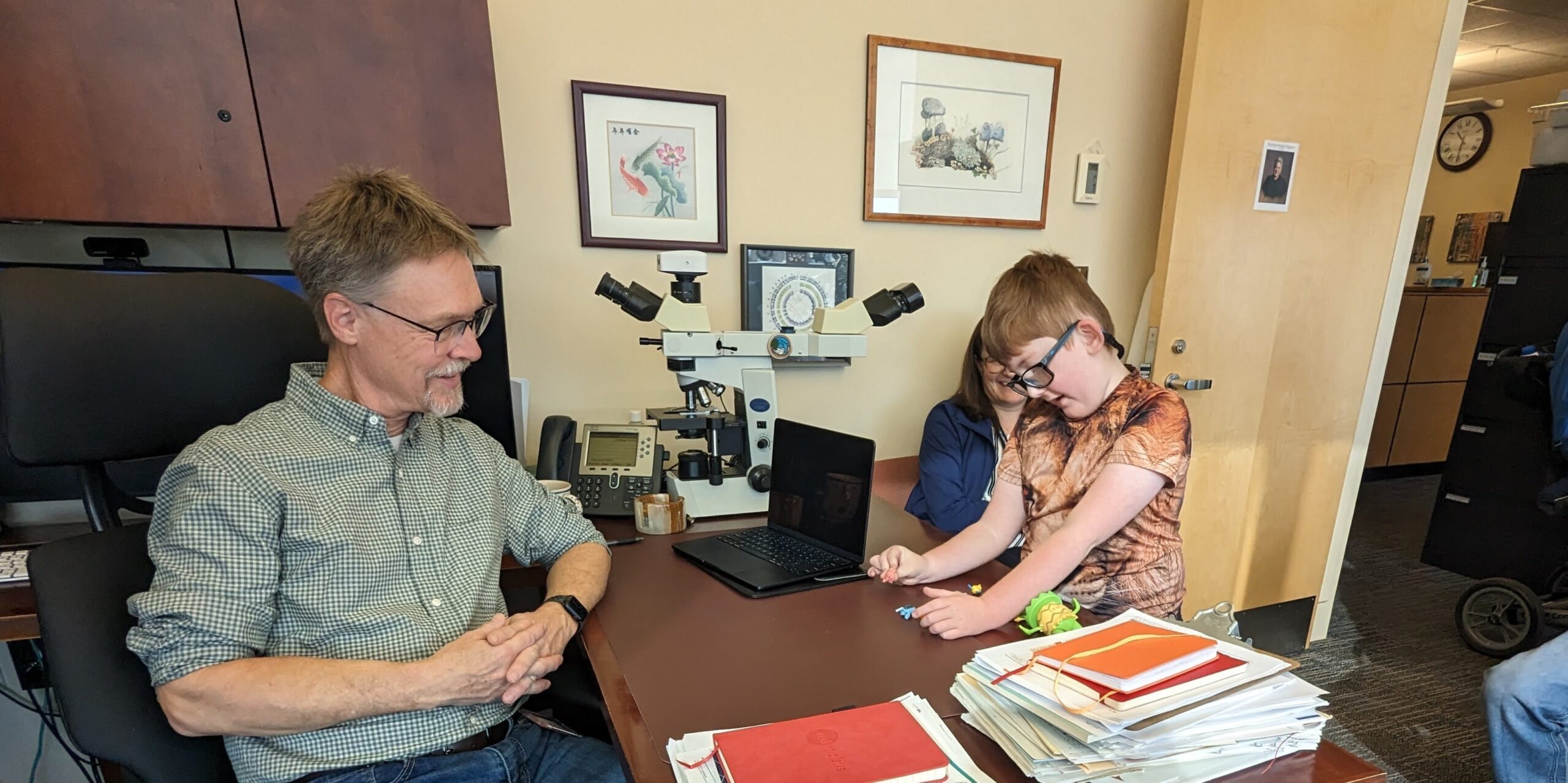 Doctor speaking with a child and caregiver in a medical office with a microscope on the desk.