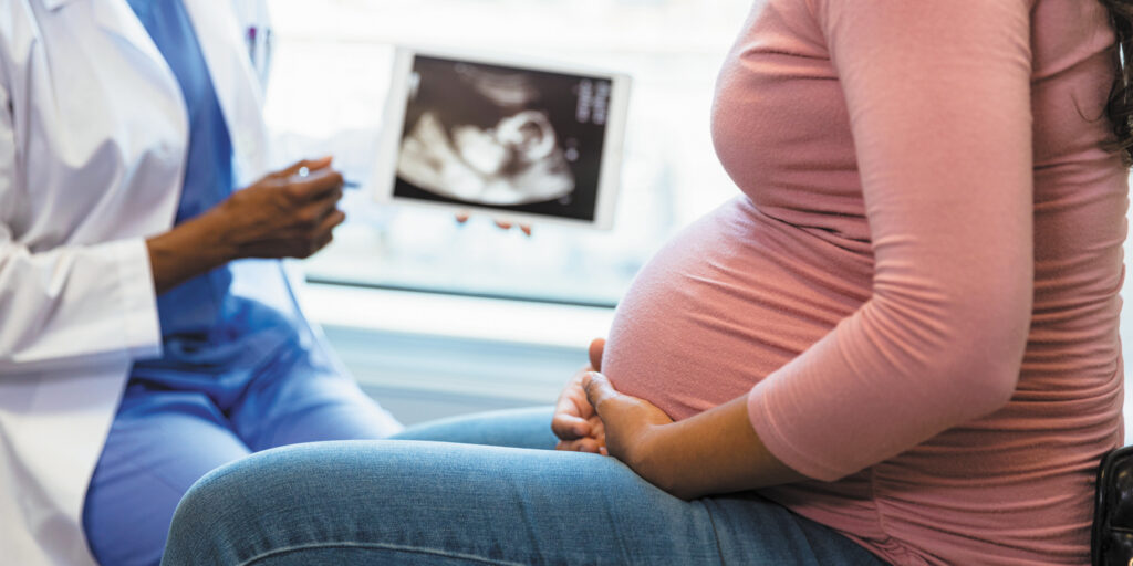 Pregnant patient consults with a healthcare provider as an ultrasound image is displayed nearby.