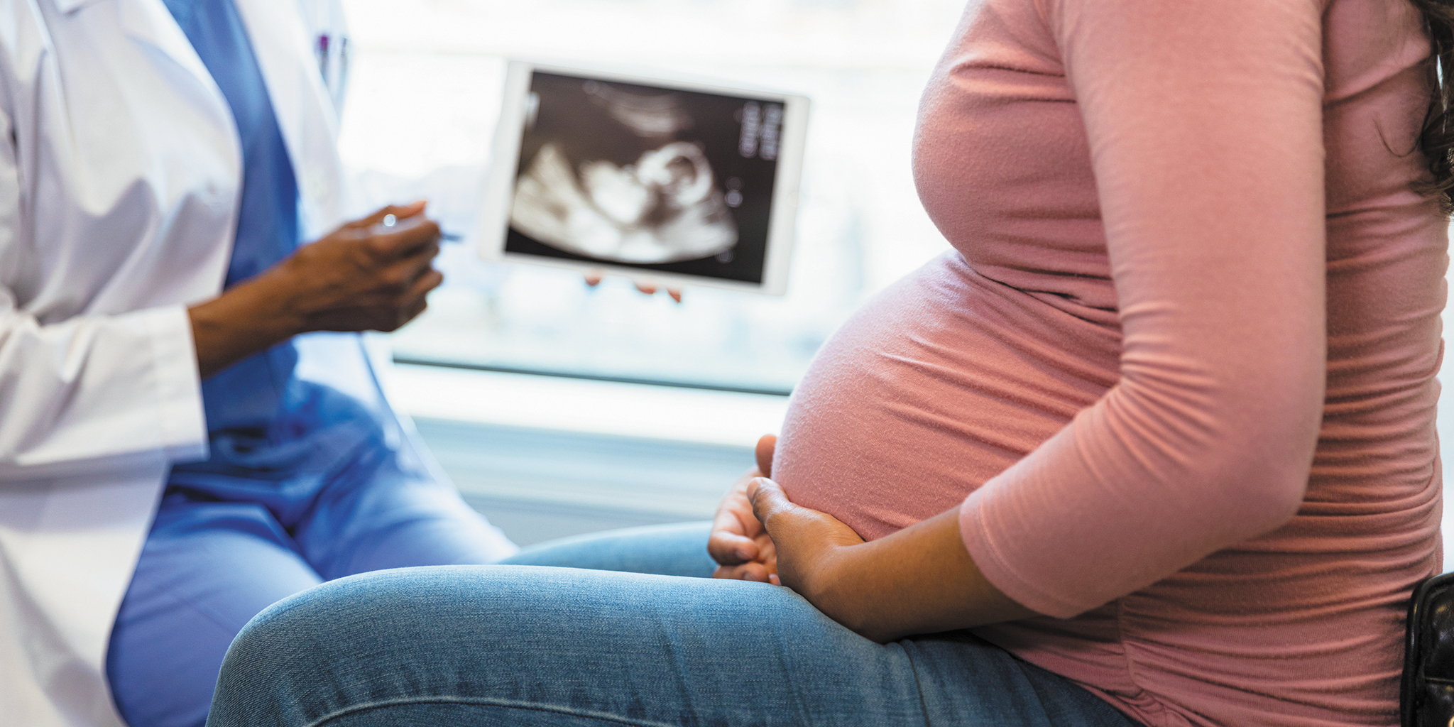 Pregnant patient consults with a healthcare provider as an ultrasound image is displayed nearby.