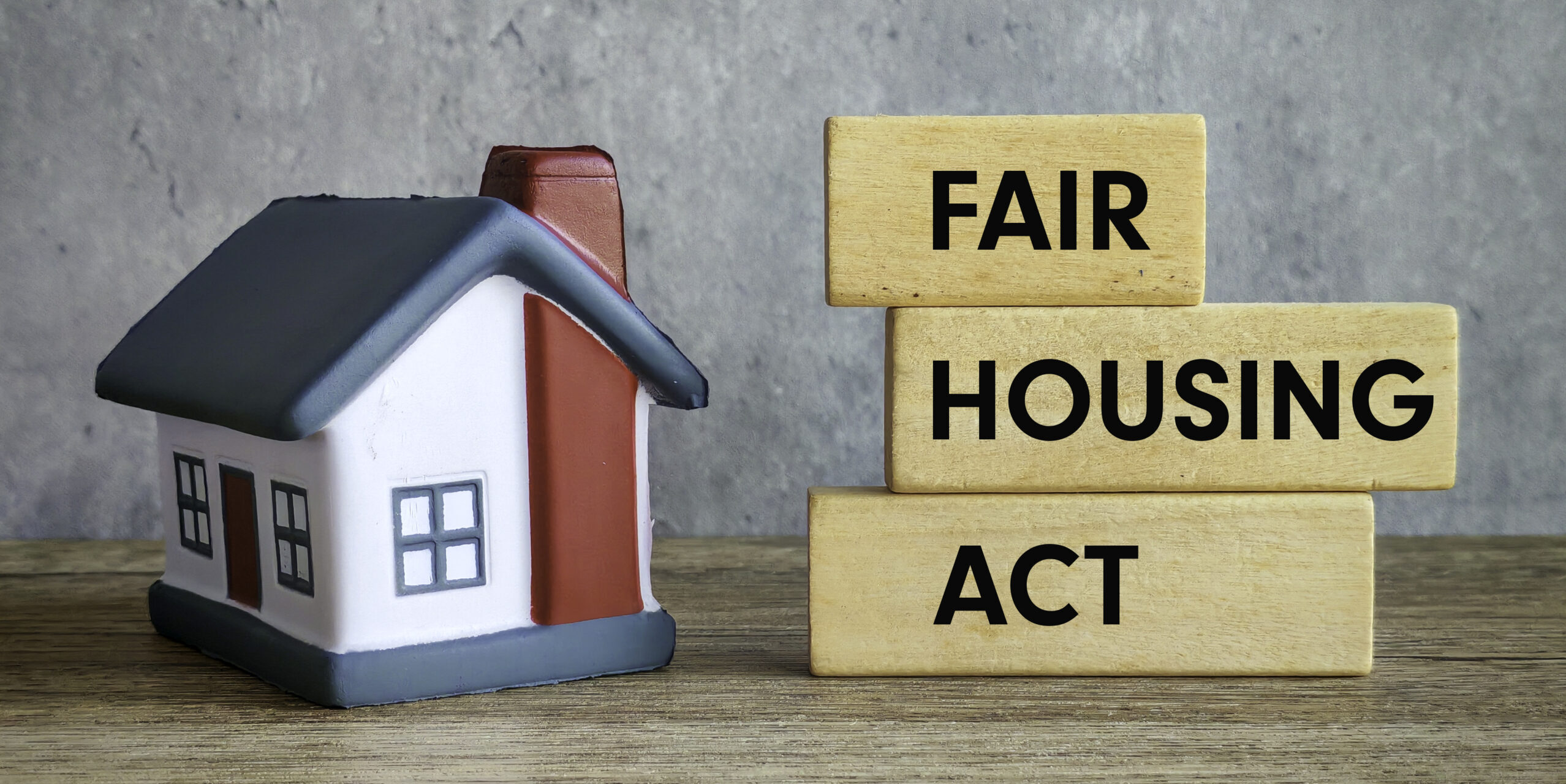 Fair Housing Act Text with Miniature House on Wooden Table and Gray Background