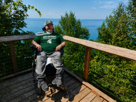 A man in a power wheelchair on a deck wearing Every Spartan apparel. 