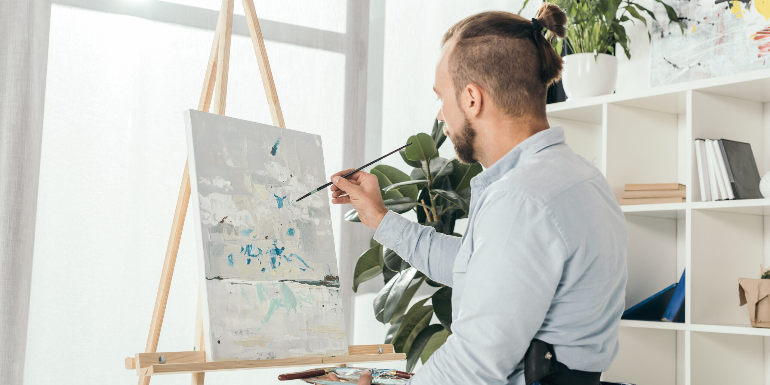 disabled man on wheelchair painting in front of window at home