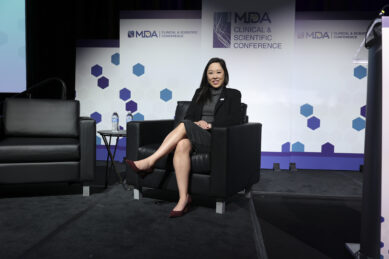 Dr. Angela Lek sits in a black chair wearing a black blazer and skirt on stage at conference